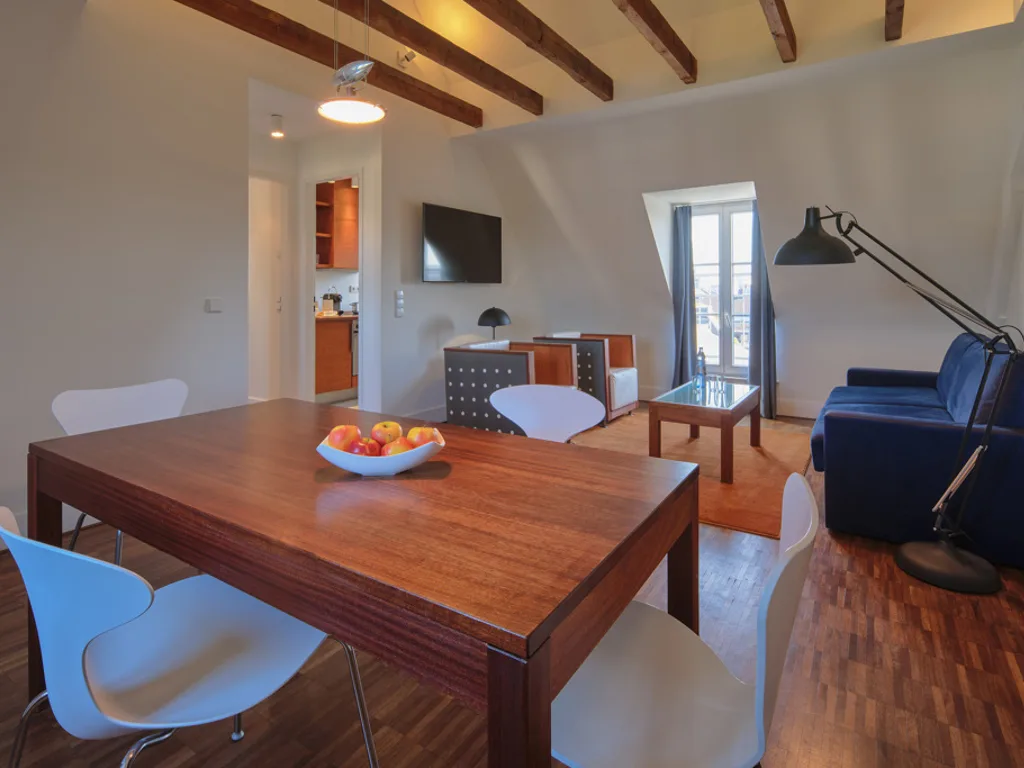 hotel-antonius-koeln-superior-apartment-5 holz-esstisch-sitzbereich-mit-blauer-couch-und-tv