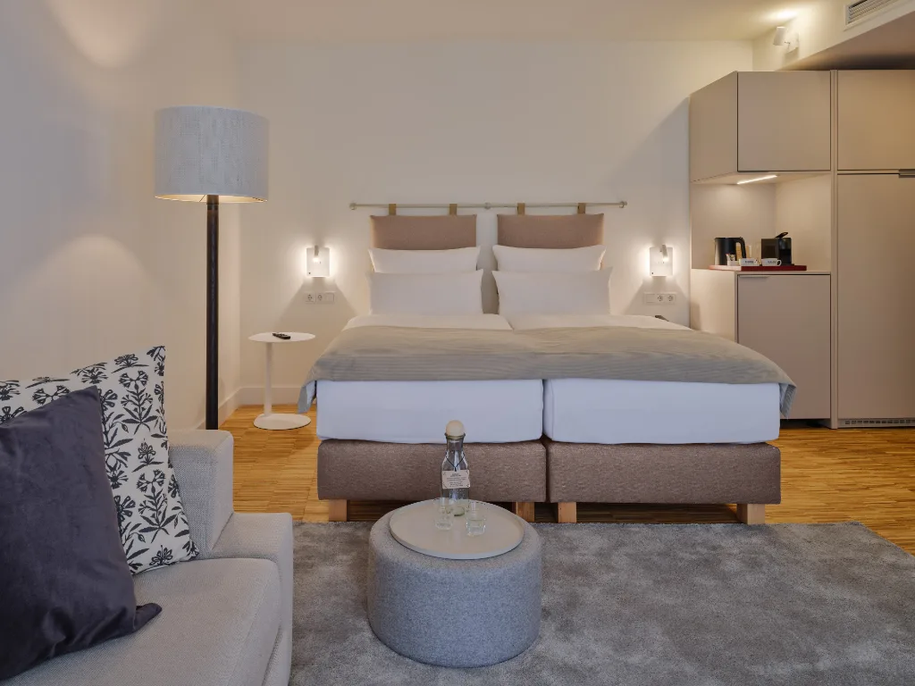 zimmer-mit-blick-auf-das-doppelbett-kleiner-beistelltisch-mit-glaskaraffe
