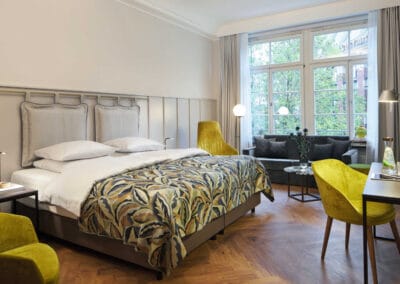 doppelbett-zwei-gelbe-sessel-eine-couch-vor-grossem-doppelfenster