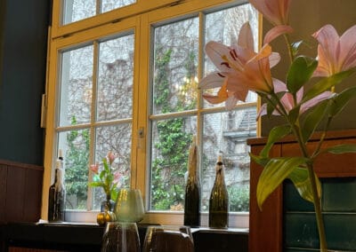 fenster-zum-hof-mit-kerzenflaschen-und-blumen