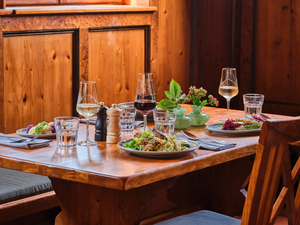 gedeckter-holztisch-im-gasthaus-mit-Speisen-auf-tellern-weinglaeser