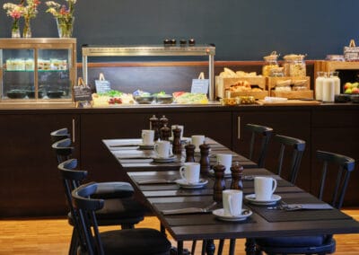 gedeckte-fruehstueckstafel-dunkle-holzmoebel-mit-blick-zum-buffet