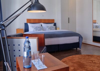 beistelltisch-mit-wasserflasche-laue-stehleuchte-bett-im-hintergrund