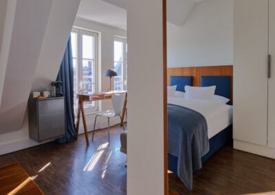 schreibtisch-am-fenster-mit-weissem-stuhl-bett-spiegelt-im-spiegel