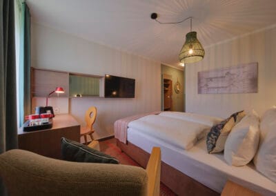 zimmer-erdfarbener-sessel-schreibtisch-mit-holzstuhl-doppelbett