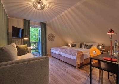 doppelbett-rot-gemusterte-tagesdecke-mintfarbene-couch-schreibtisch-schreibtischlampe-bodentiefe-fenster