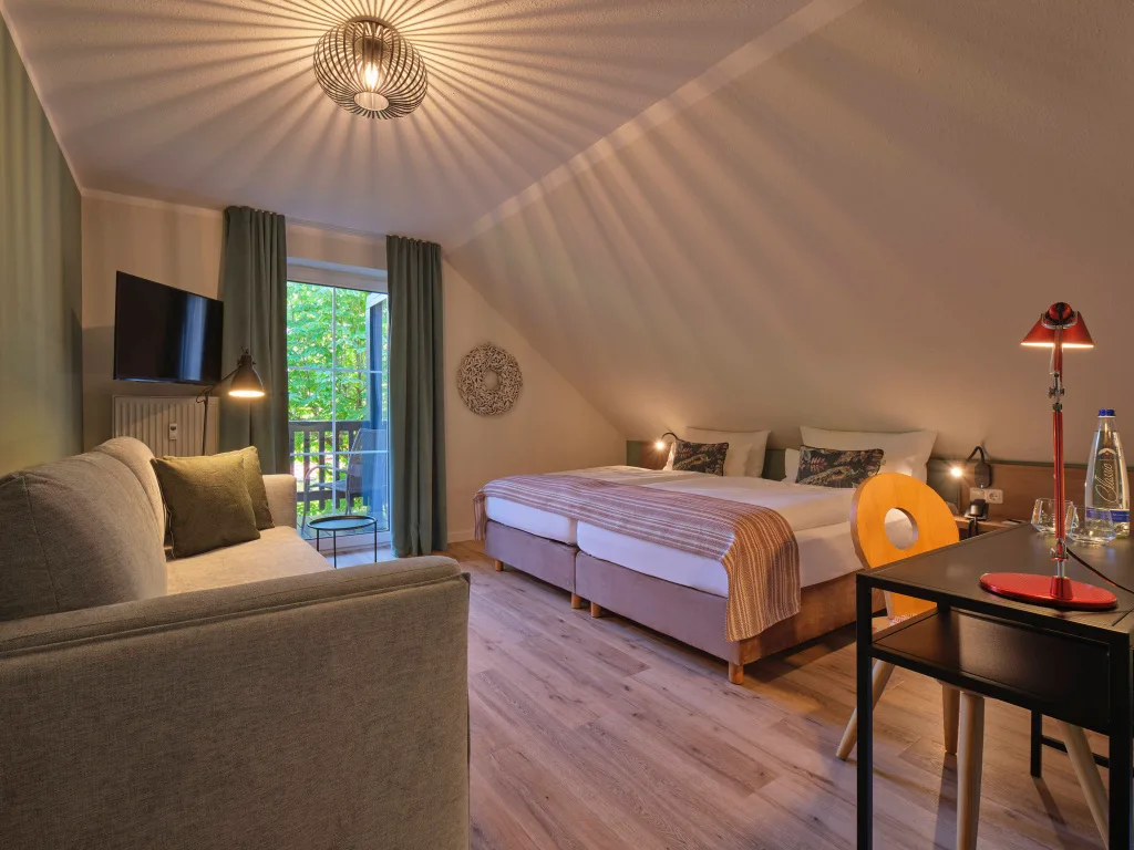 doppelbett-rot-gemusterte-tagesdecke-mintfarbene-couch-schreibtisch-schreibtischlampe-bodentiefe-fenster