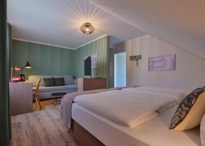 zimmer-doppelbett-couch-komode-mit-tv-gruene-tapete-schreibtisch