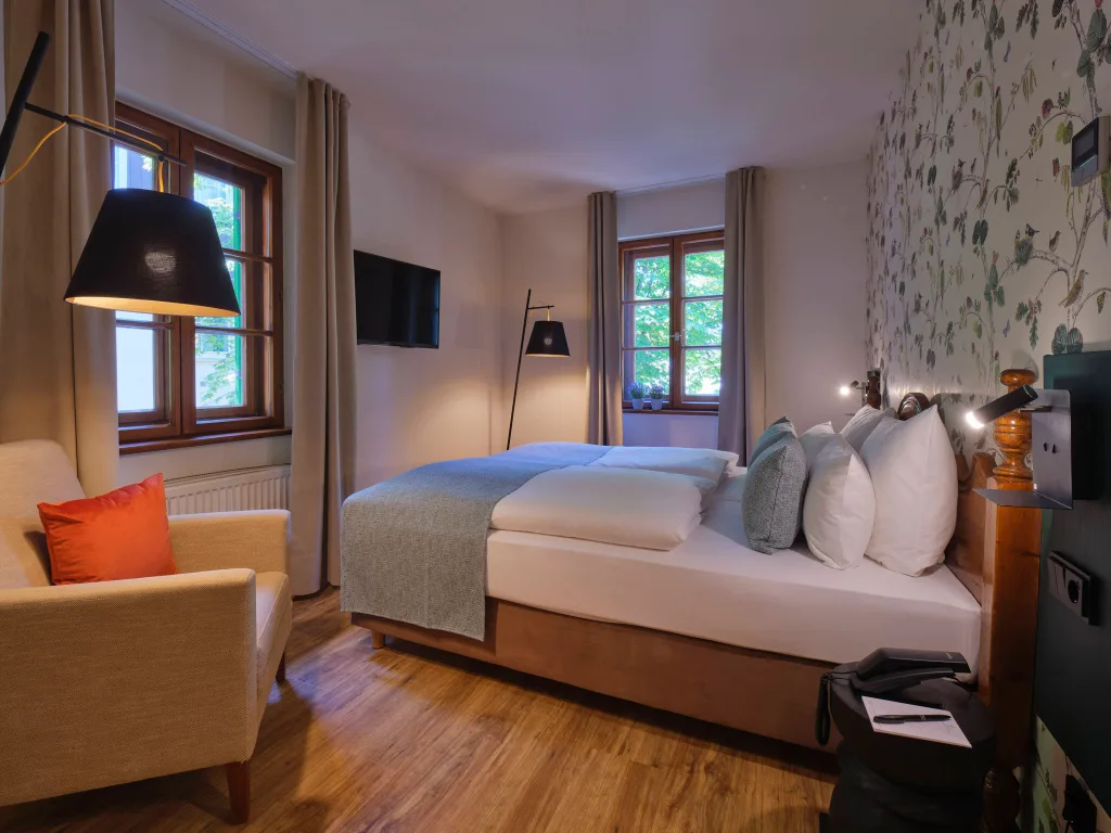 doppelbett-und-sessel-in-hell-tapezierten-zimmer-massivholz