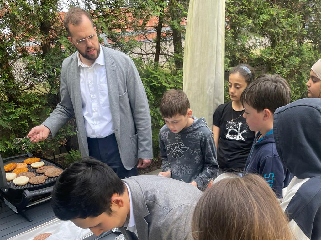 Erwachsener grillt und Kinder schauen zu.