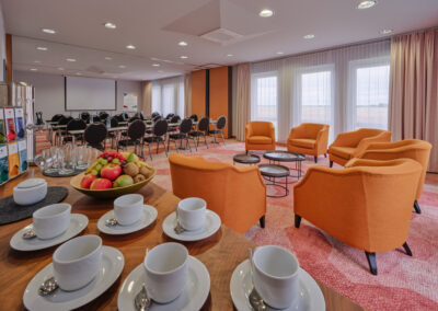 tagungsraum-kaffeetassen-auf-anrichte-orangene-sessel-parlamentarische-bestuhlung
