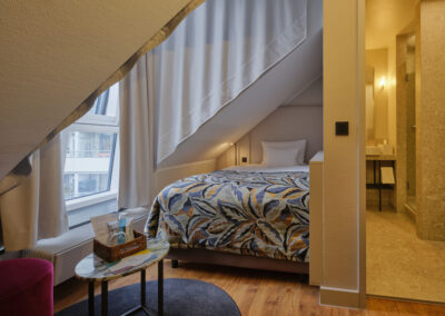 einzelbett-unter-dachschraege-marmor-beistelltisch-blick-ins-bad