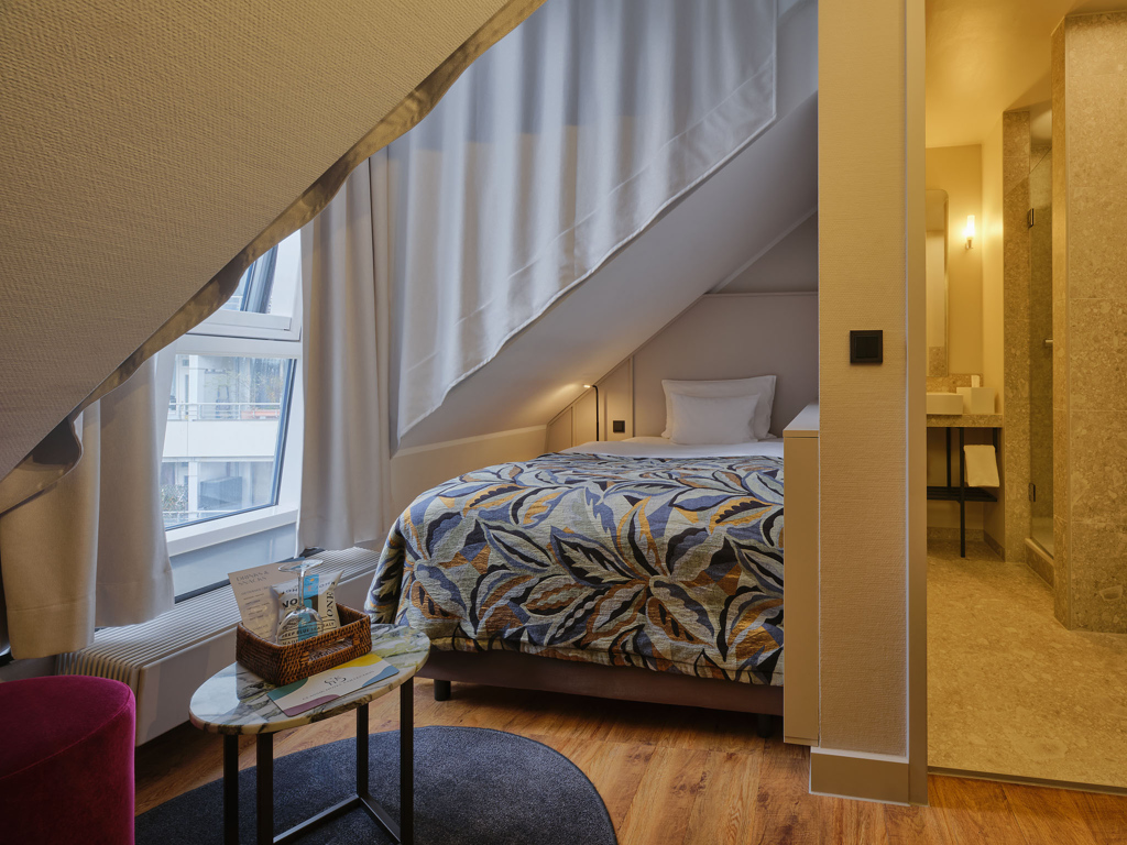 einzelbett-unter-dachschraege-marmor-beistelltisch-blick-ins-bad