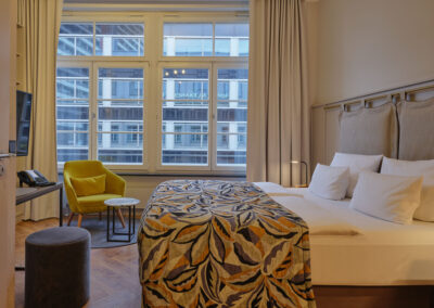 doppelbett-bunte-tagesdecke-gelber-sessel-grosse-fenster