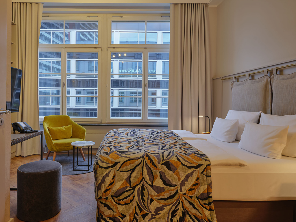 doppelbett-bunte-tagesdecke-gelber-sessel-grosse-fenster