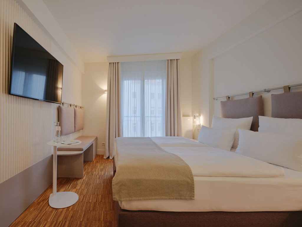 weiss-bezogenes-doppelbett-sitzbank-tv