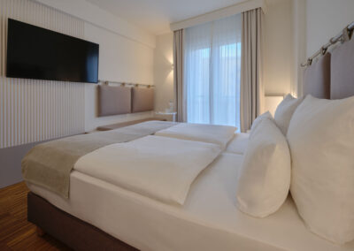 seitlicher-blick-ins-zimmer-doppelbett-sitzbank-tv