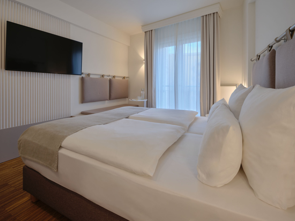 seitlicher-blick-ins-zimmer-doppelbett-sitzbank-tv